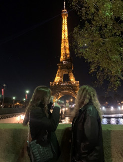 Ilanah and friend posing for picture while looking at the lit up Eiffel Tower at night