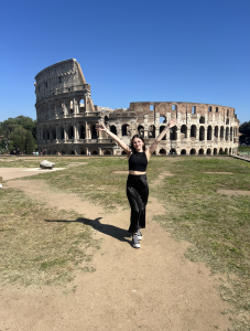 Brynn with arms up in the air standing in front of the Roman Coliseum 