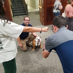 Man poses with Butler Blue as woman directs Butler Blue's attention while another man takes picture.